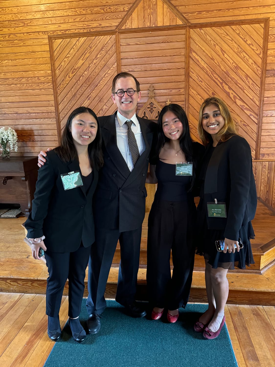 Ava and two fellow Coolidge Senators, all in black formalwear with green Coolidge Foundation badges, standing with a speaker in a suit inside the wood-panelled Union Christian Church at Plymouth Notch.