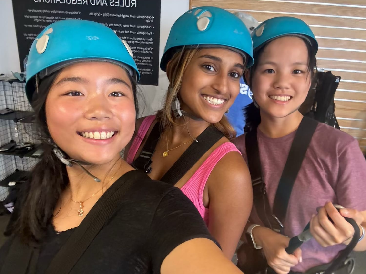 Three Senators in blue climbing helmets and harnesses grinning before their turn on the zip line.