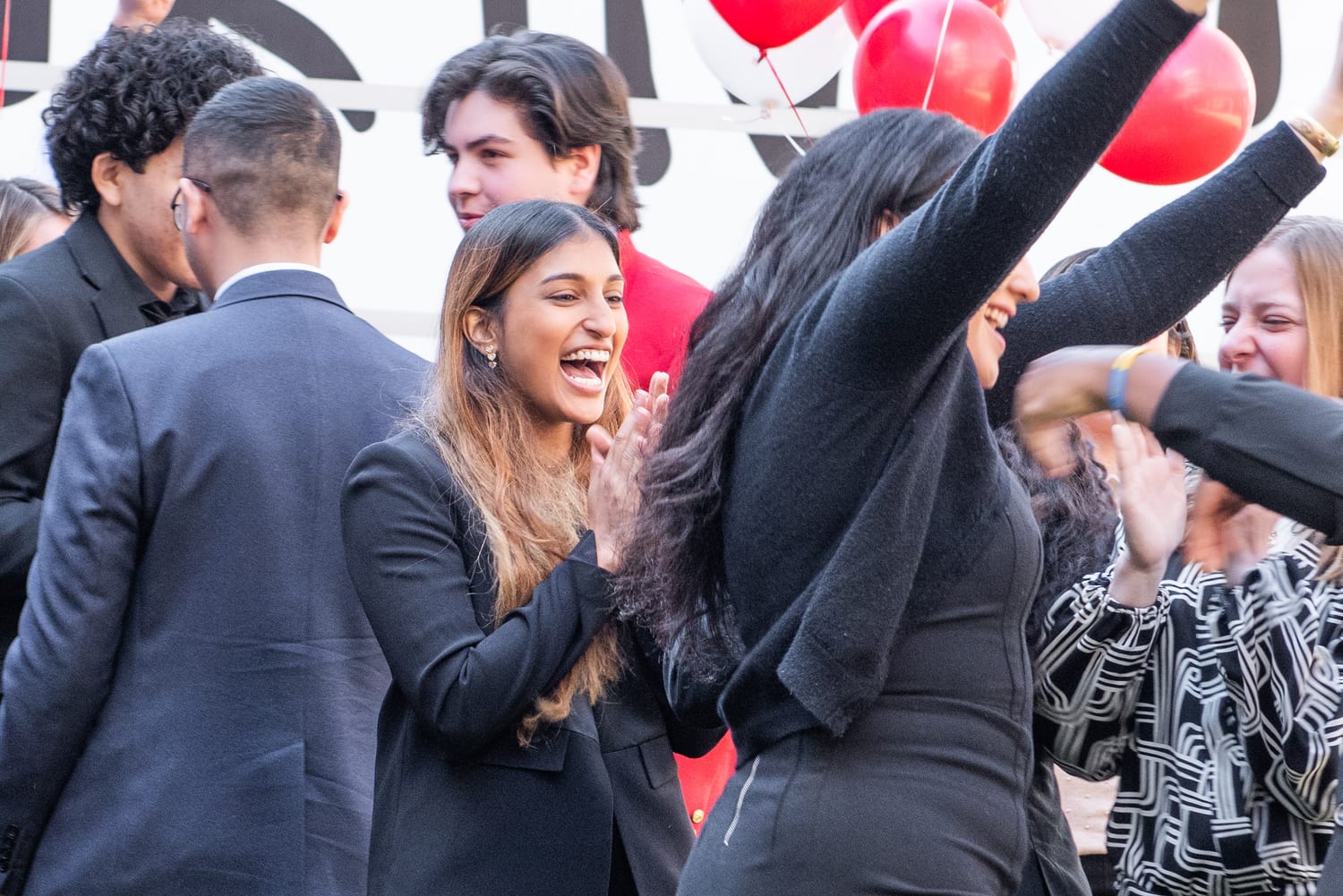 Ava laughing and clapping among fellow scholars as red and white balloons and a raised arm shoot up in celebration.