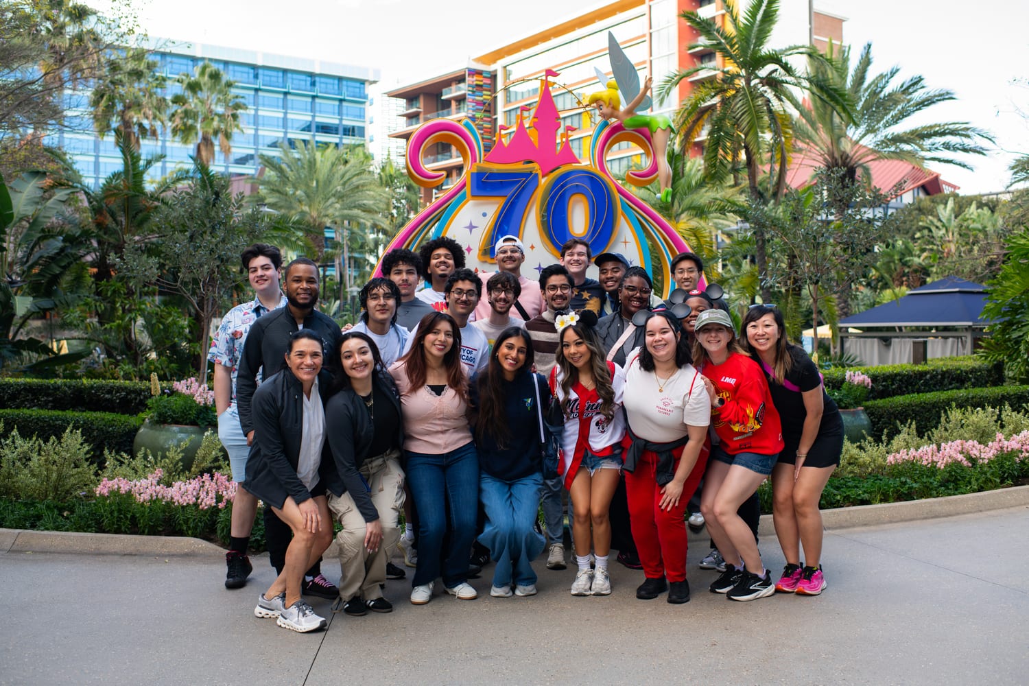 The whole cohort and program staff posed in front of a large Disneyland 70th-anniversary “70” display topped with Tinker Bell, palms behind them.