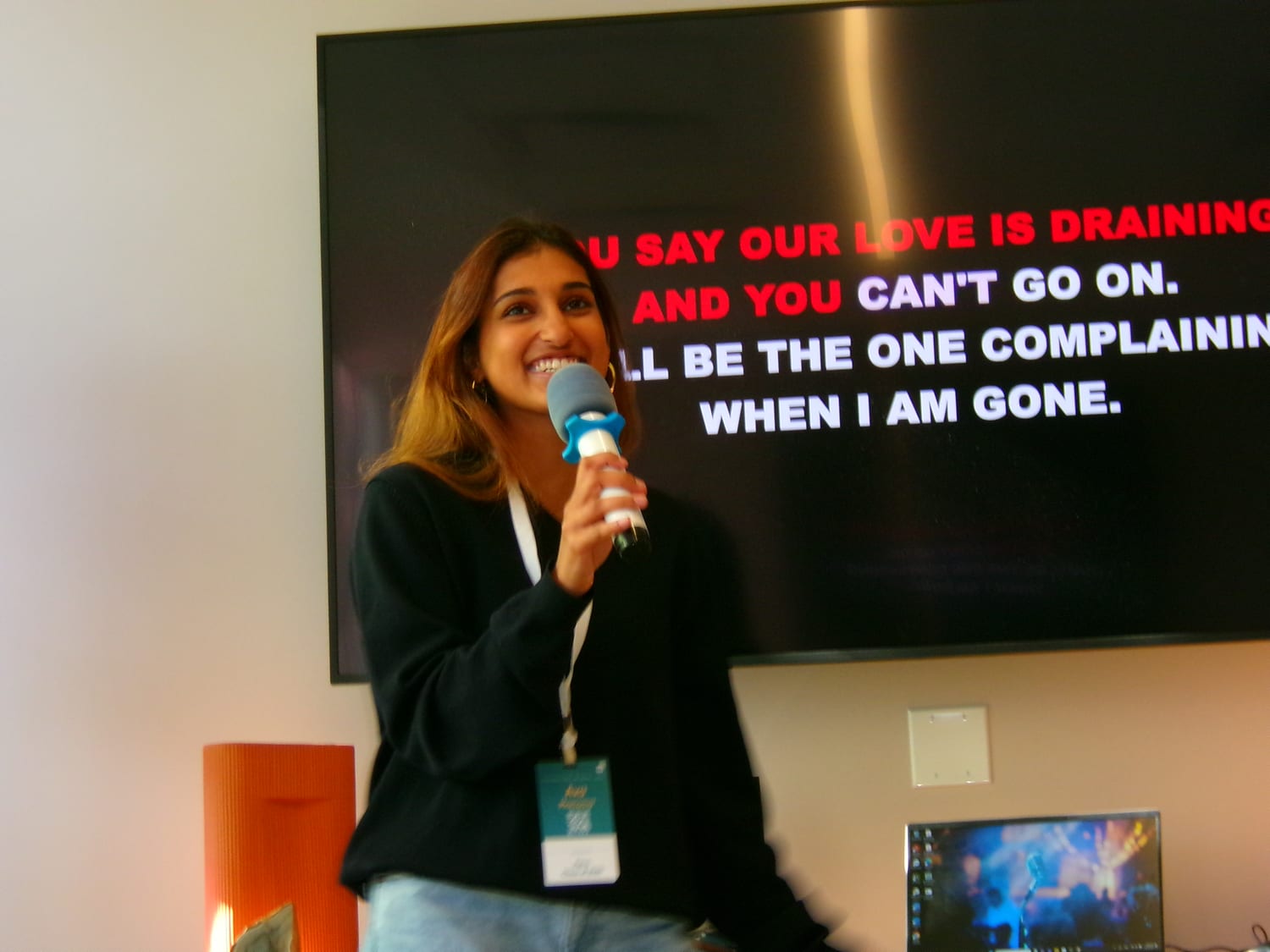 Ava laughing mid-song with a blue karaoke microphone, standing in front of a screen scrolling red-and-white karaoke lyrics.