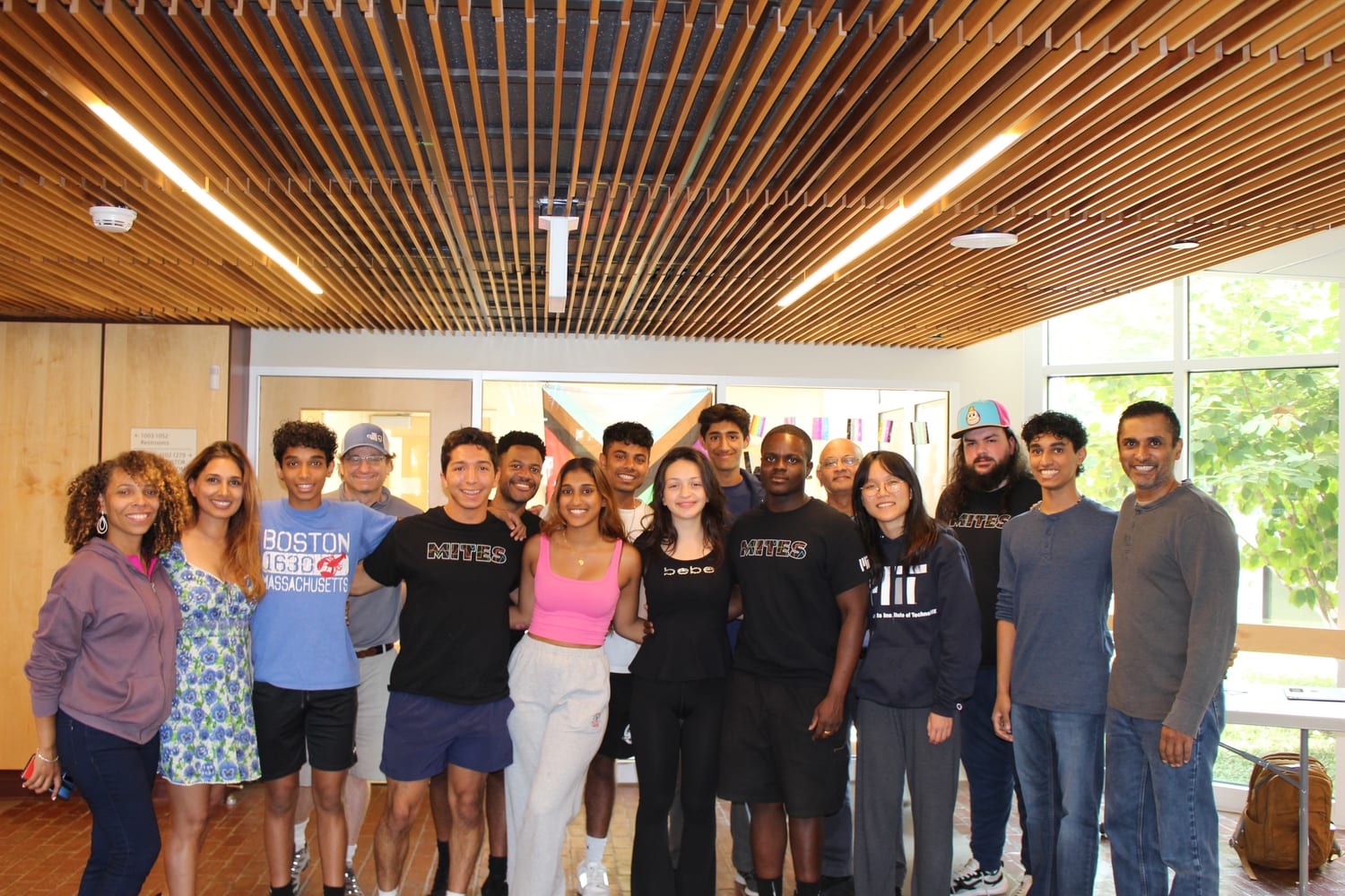 The MITES students and instructors together in a slatted-timber lobby, several wearing MITES and MIT shirts.