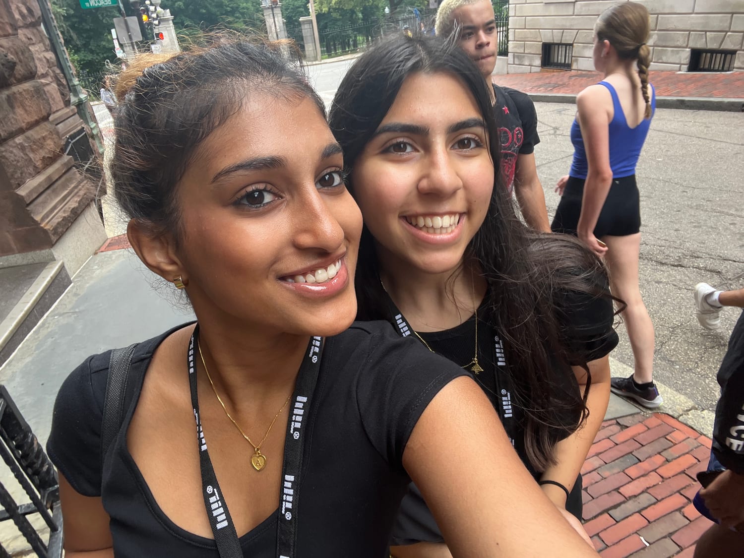 Ava and a fellow MITES student taking a selfie on a Boston street in MITES lanyards, brownstones behind them.