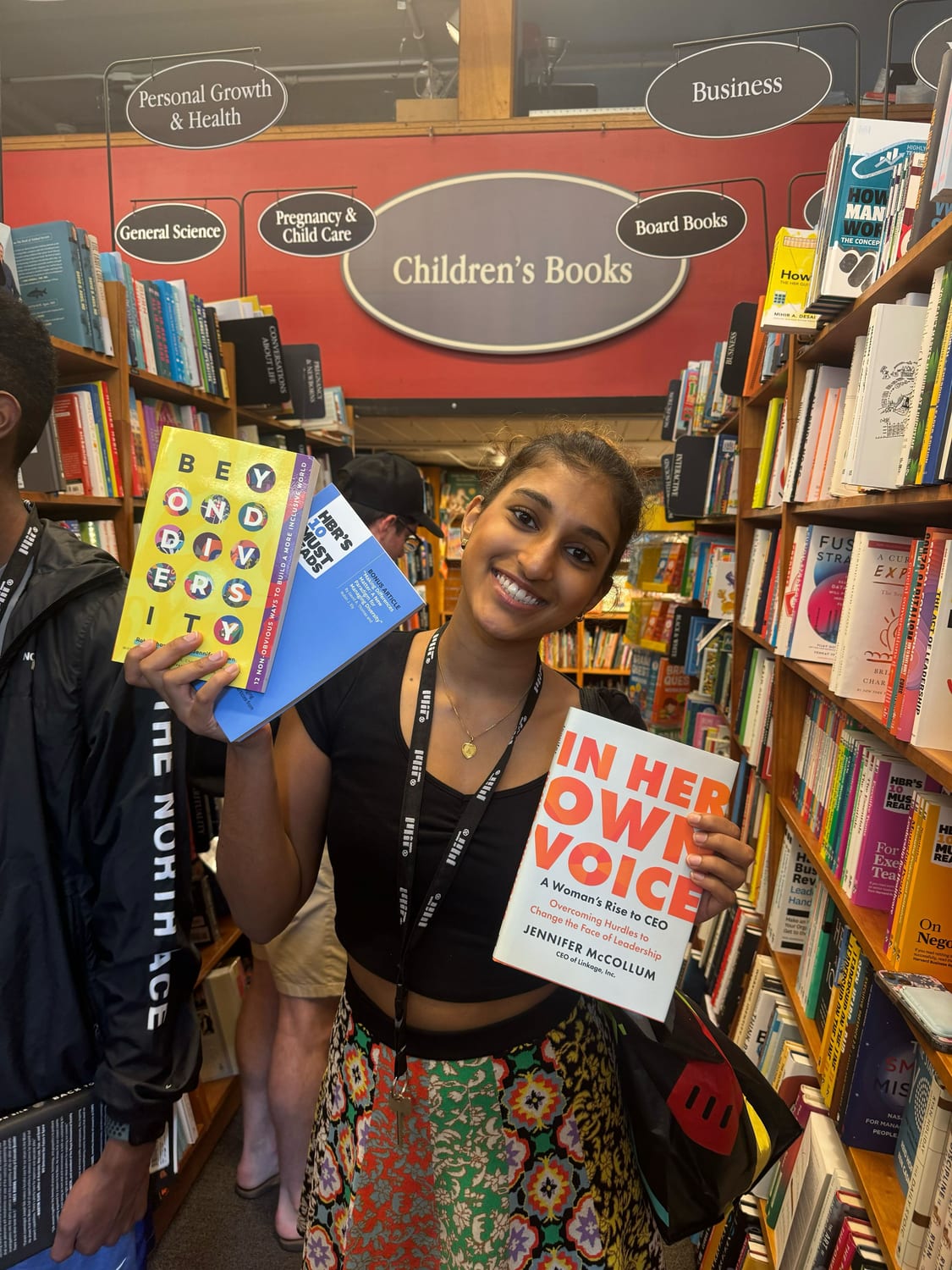 Ava in a bookshop holding up three books — Beyond Diversity, HBR’s 10 Must Reads, and In Her Own Voice: A Woman’s Rise to CEO.