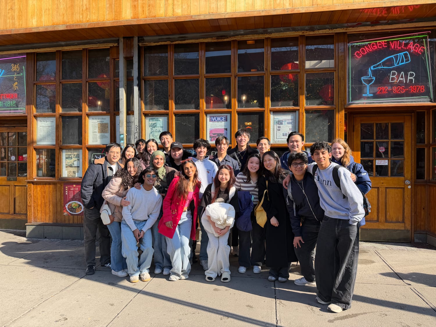 About twenty members squeezed together on the pavement outside Congee Village, its neon bar sign and framed newspaper clippings filling the windows behind them.