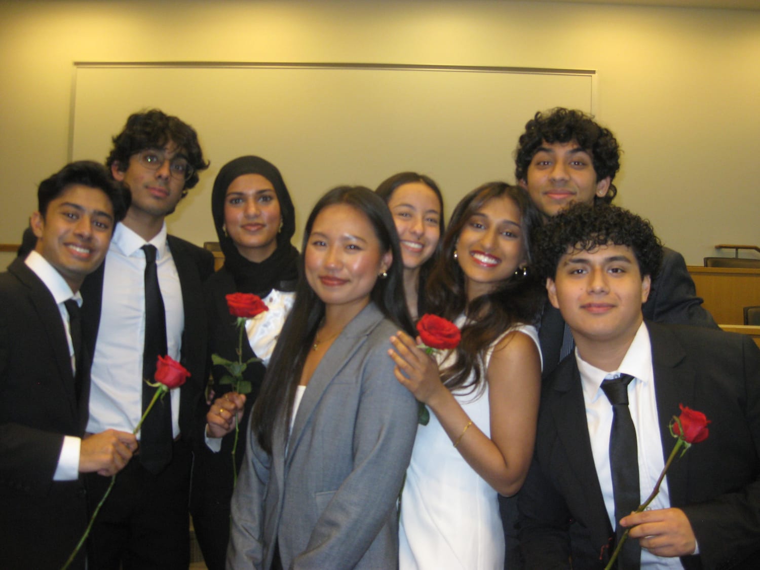 Eight new members in business formal pressed together for a photo at the front of the initiation room, most of them holding a red rose.