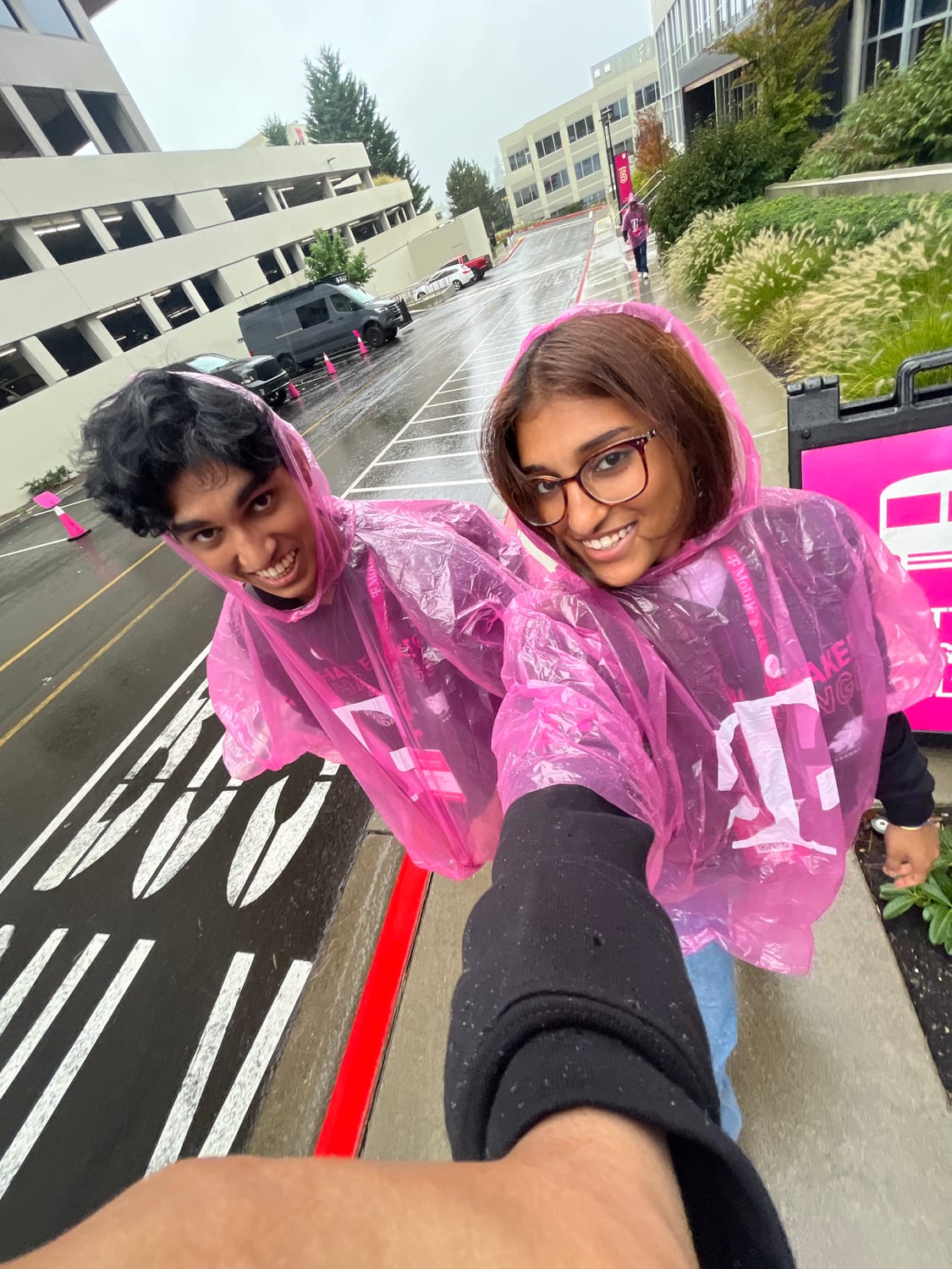 Ava and a fellow changemaker in pink T-Mobile rain ponchos taking a selfie in the rain on campus.