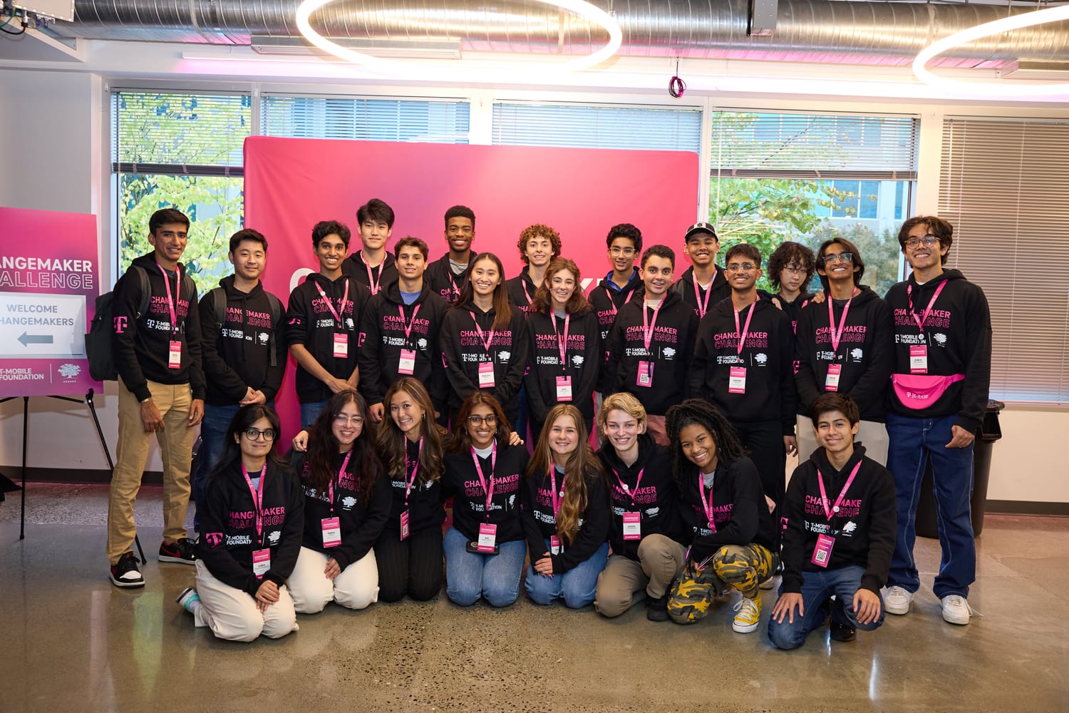 The 2023 Changemaker Challenge cohort in matching hoodies in front of a pink “Welcome Changemakers” backdrop.