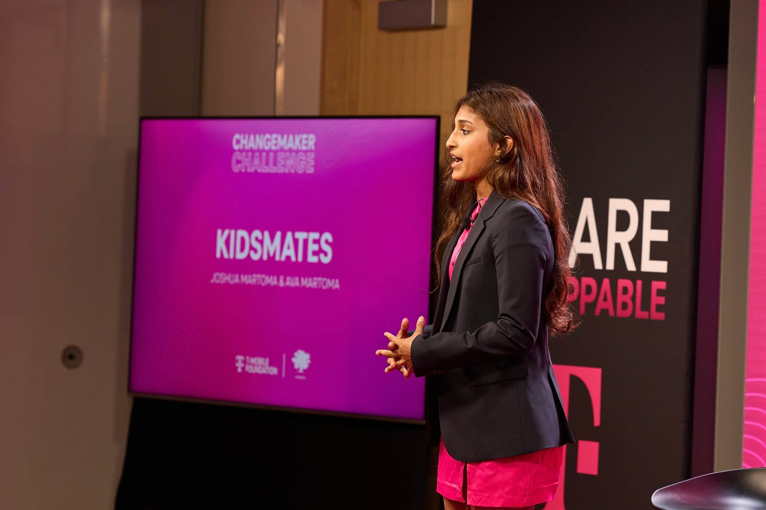 Ava pitching KIDSMATES on stage, with a slide reading “KIDSMATES — Joshua Martoma & Ava Martoma” behind her.