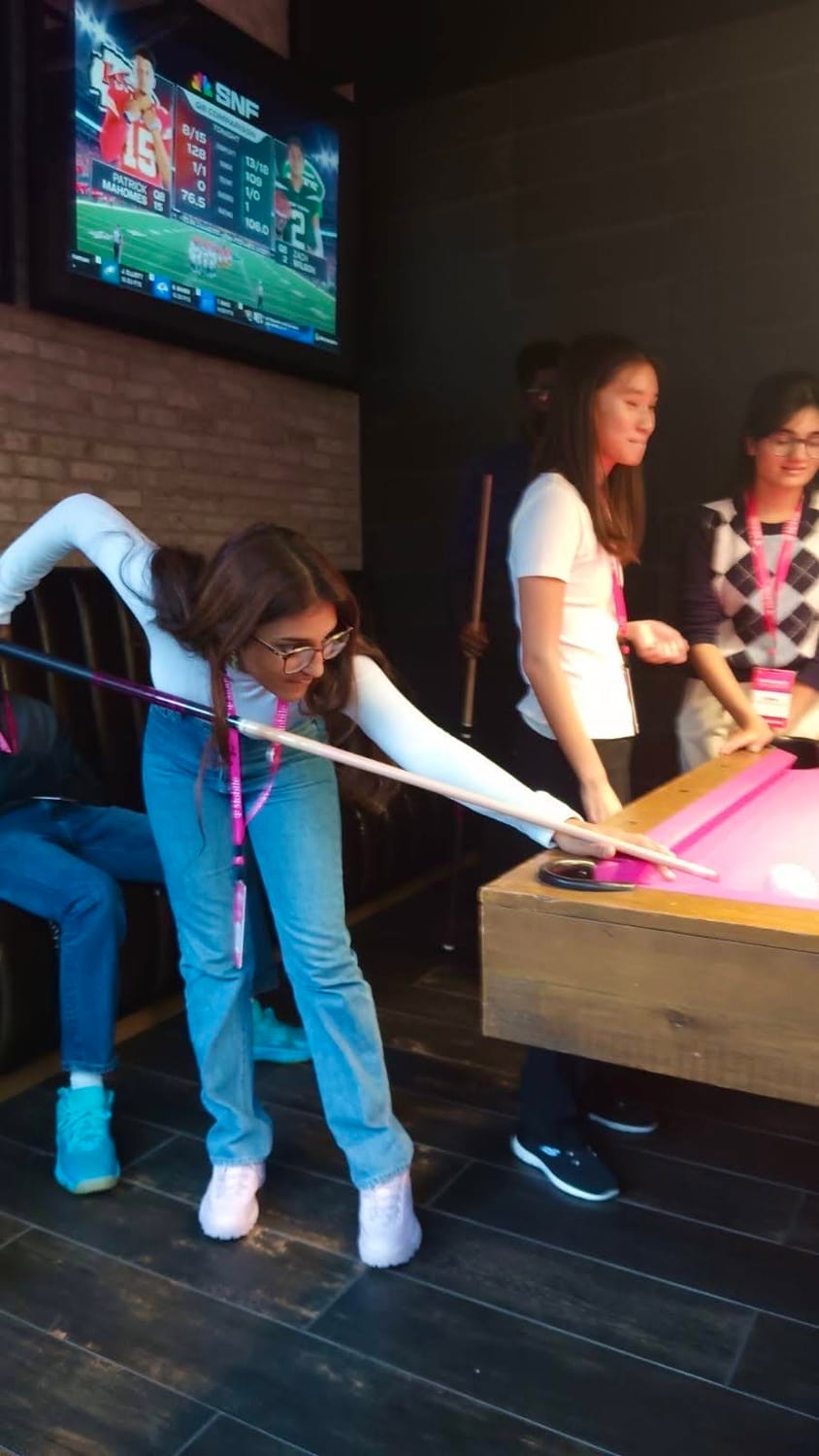 Ava lining up a shot on a pink-felt pool table during downtime.