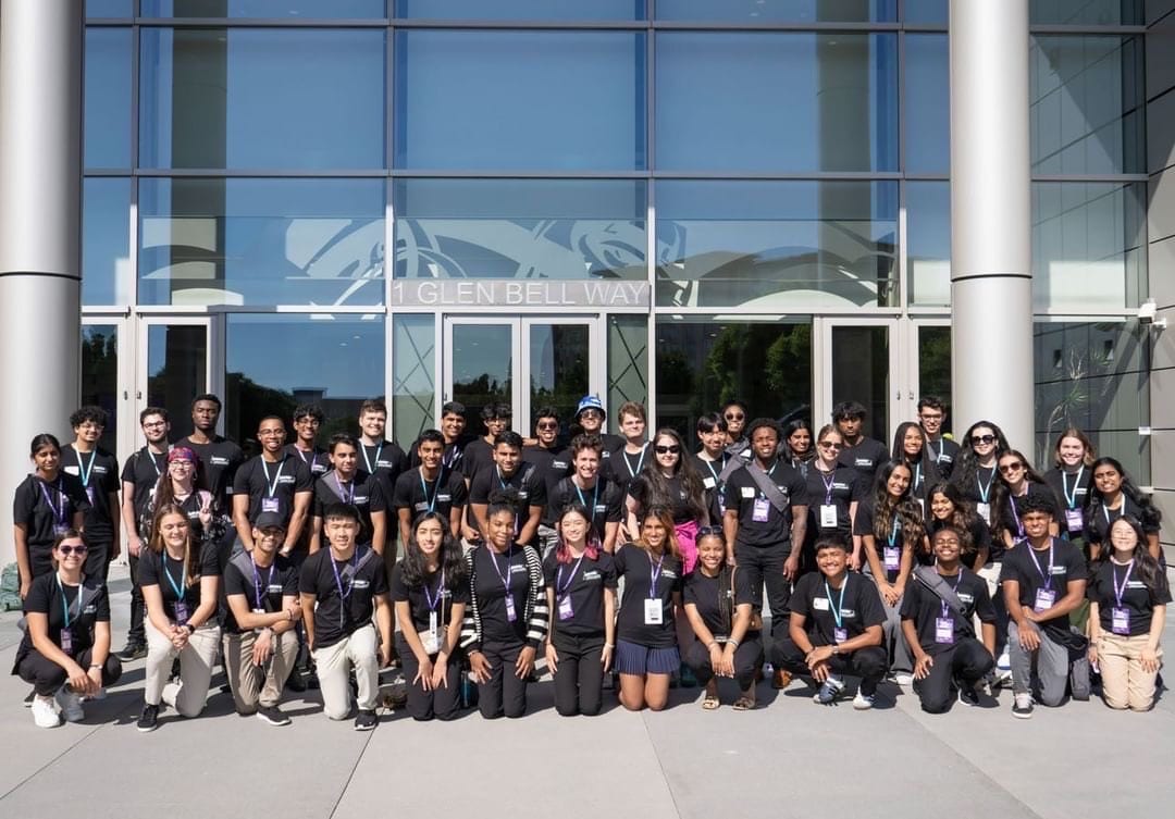 The full Ambition Accelerator cohort of about fifty people in matching black T-shirts and purple lanyards, posed outside the glass entrance of Taco Bell headquarters.