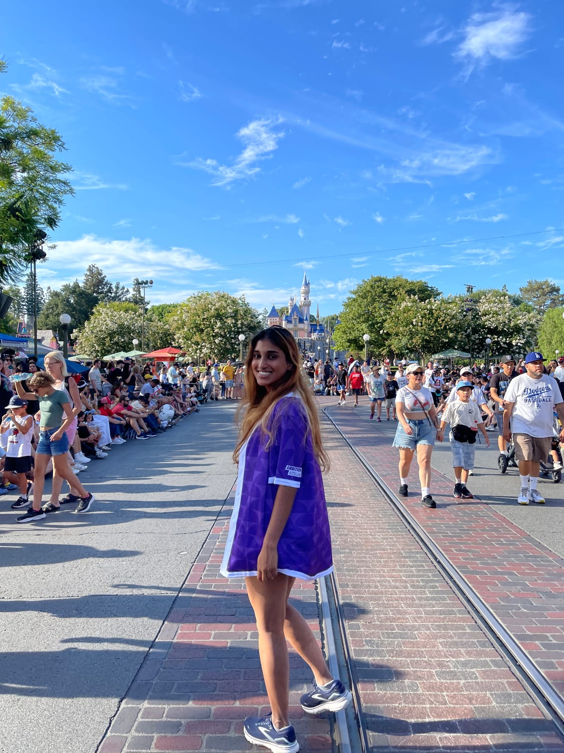 Ava in a purple Ambition Accelerator jersey standing on the tram tracks on Main Street, U.S.A., with Sleeping Beauty Castle in the distance.