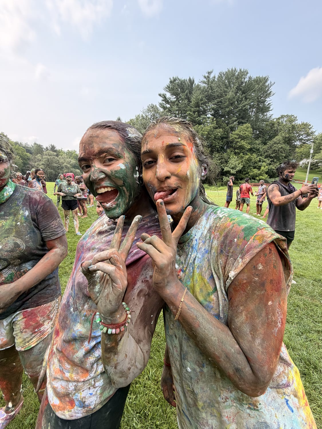 Two counselors head to head after the camp colour games, faces and clothes completely coated in green, red and white paint, throwing peace signs.