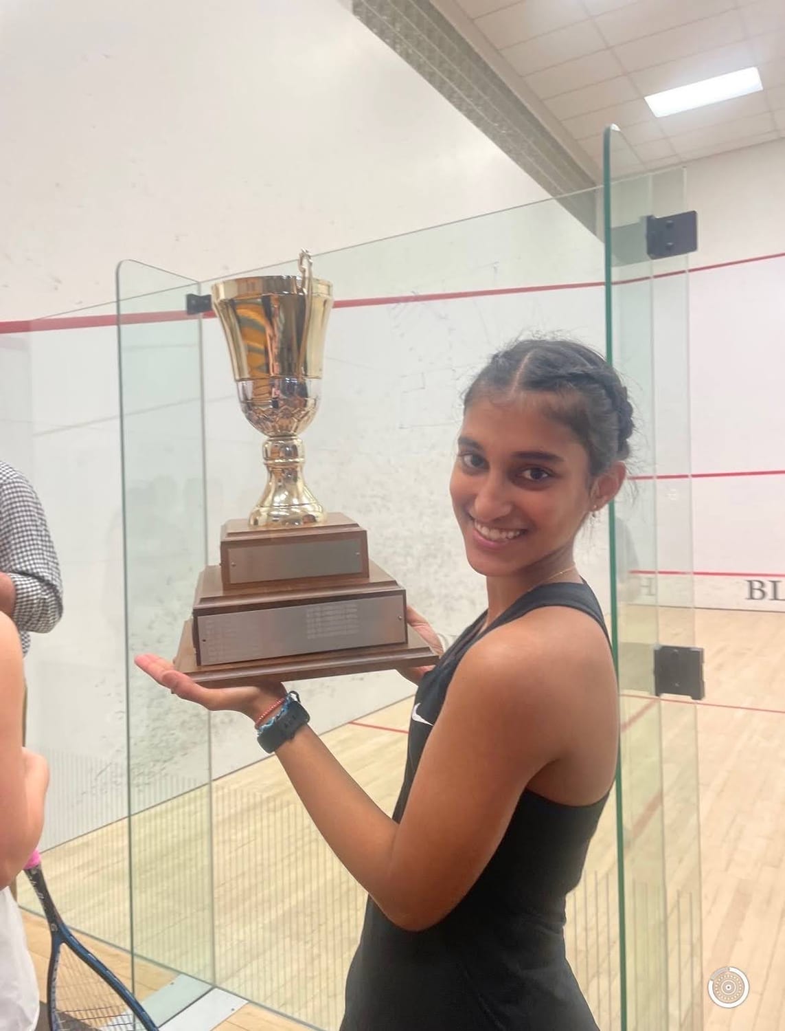 Ava holding a squash trophy on a glass court