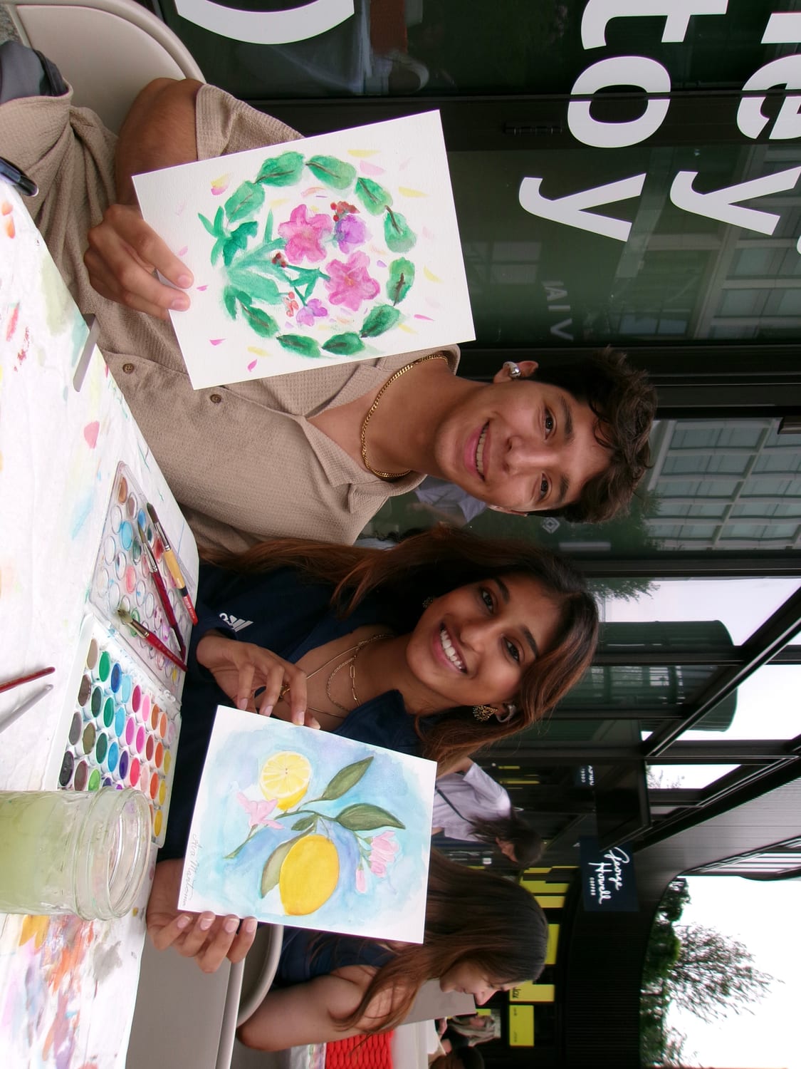 Ava and a friend showing off watercolor paintings at an outdoor paint session