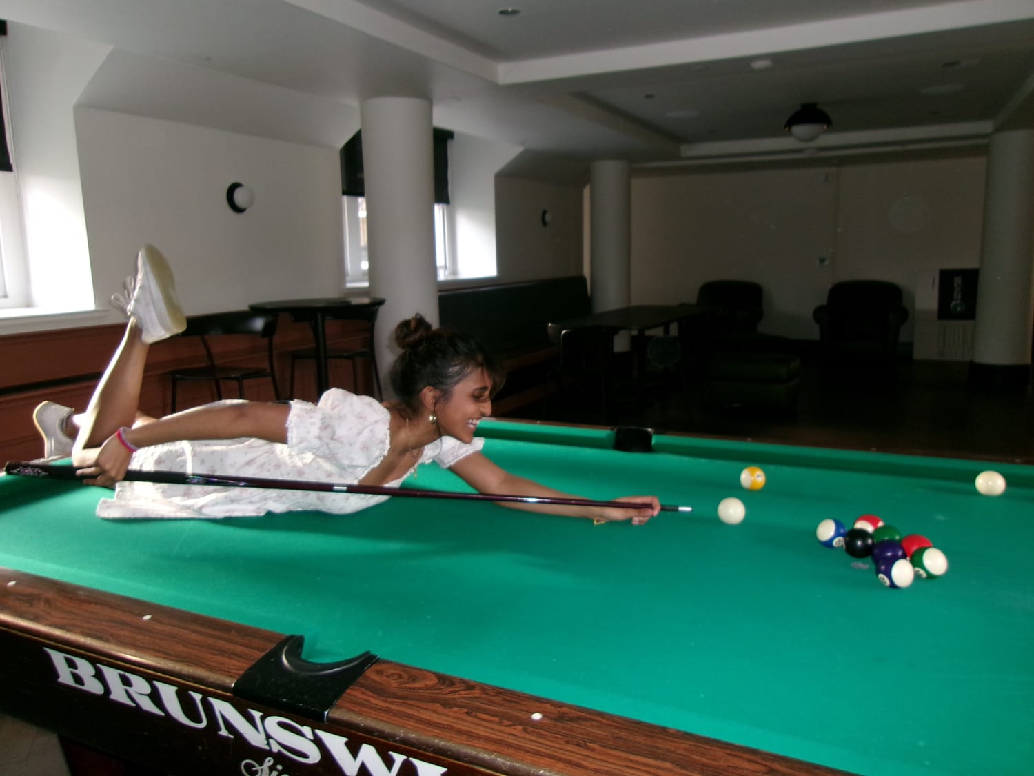 Ava lining up a shot on a pool table in a white dress
