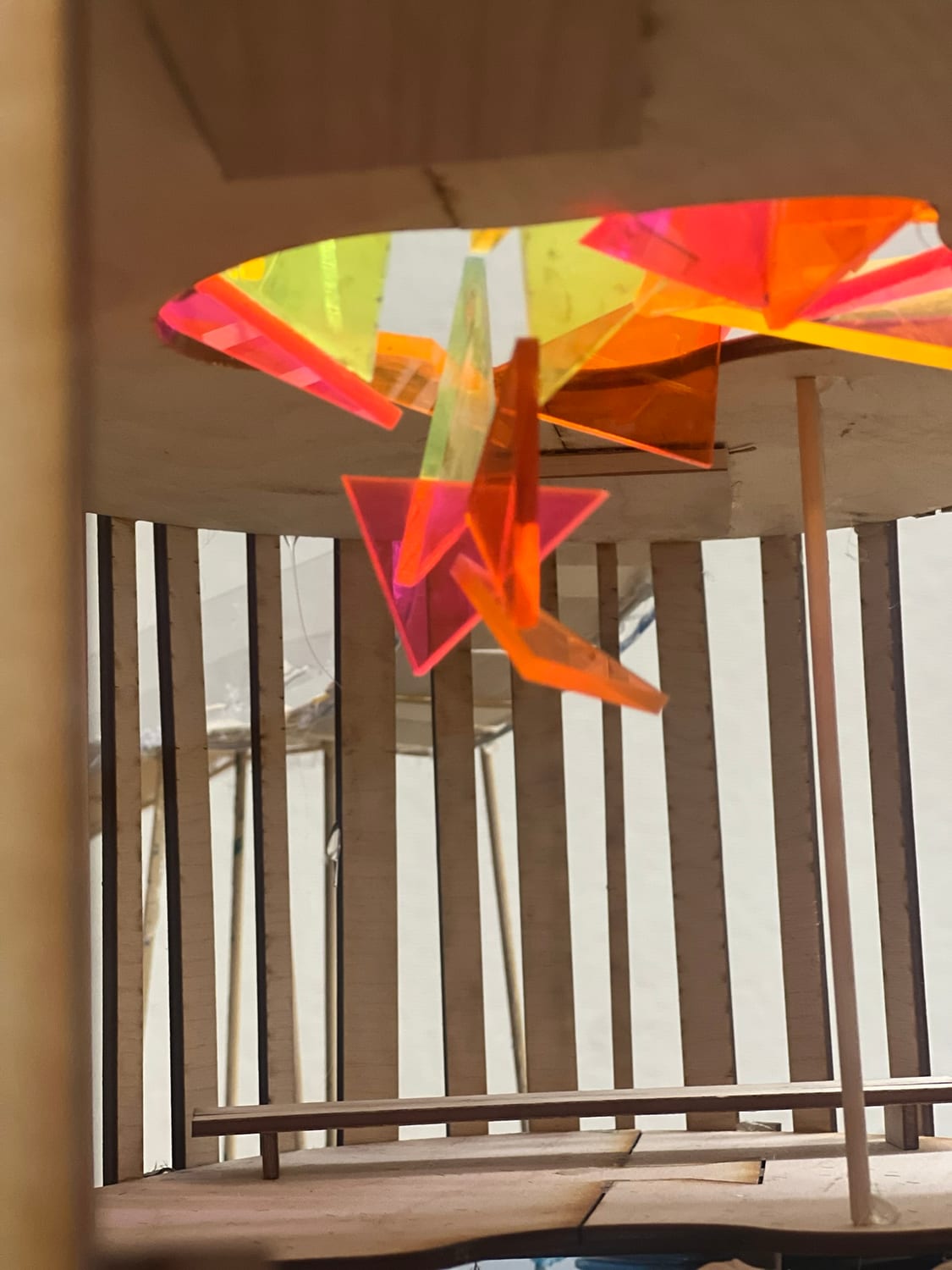 Detail of the recycled stained-glass light fixture, a cluster of pink, orange, and yellow panels suspended beneath the roof opening.