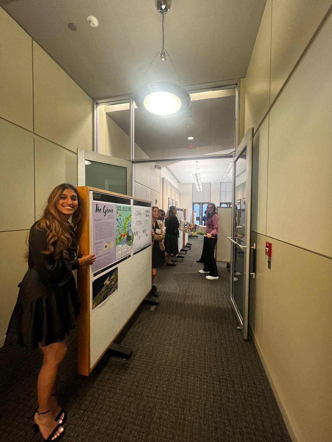 Ava beside the finished boards in the corridor of pinned-up projects before the review.