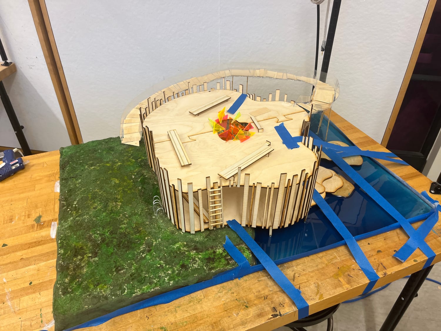 Work in progress on the bench — the model taped down with blue painter's tape while the acrylic river and terrain base set.