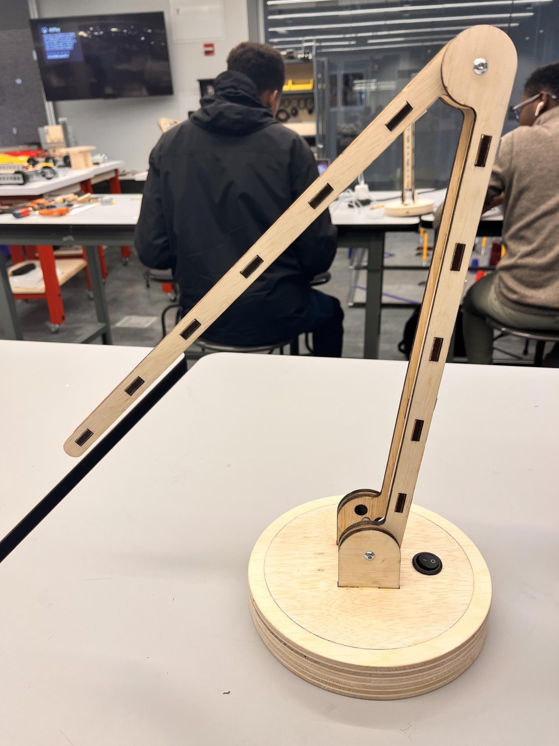 The finished LED lamp — a laser-cut plywood arm with rectangular cutouts, jointed to a stacked-ply round base with an on/off switch.