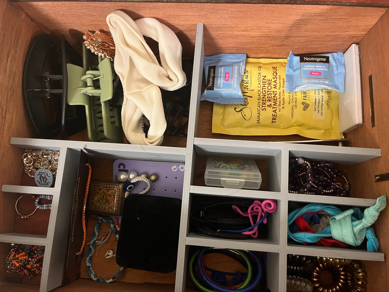 Top-down on the 3D-printed dividers in use — rings, hair ties, scrunchies and necklaces each sorted into their own cell, beside a tray of hair clips and a headband.
