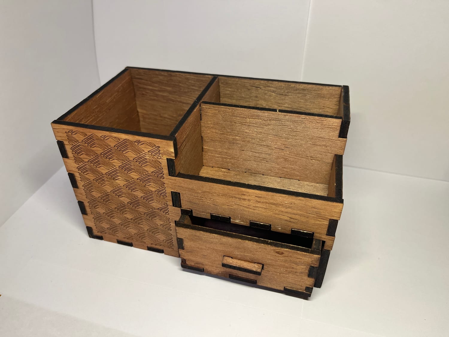 The finished pencil box: laser-cut plywood with a chevron-engraved end panel, open bays, and a pull-out drawer with a tab handle.