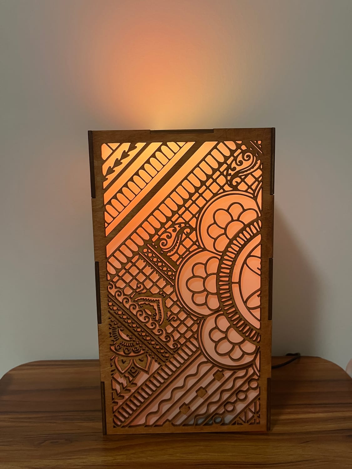 The finished luminary lit from within — warm light pushing out through the mehndi fretwork so the cut-away negative space becomes the pattern.