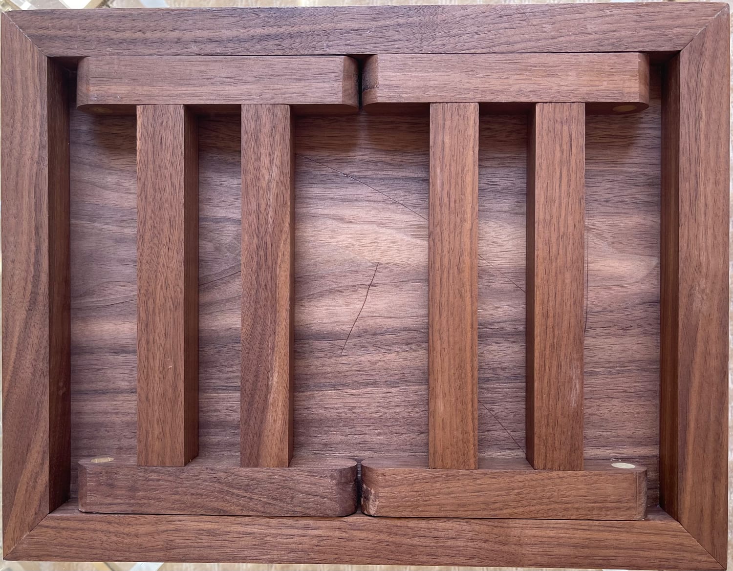The underside with the legs folded flat, nesting between walnut rails on dowel pivots.