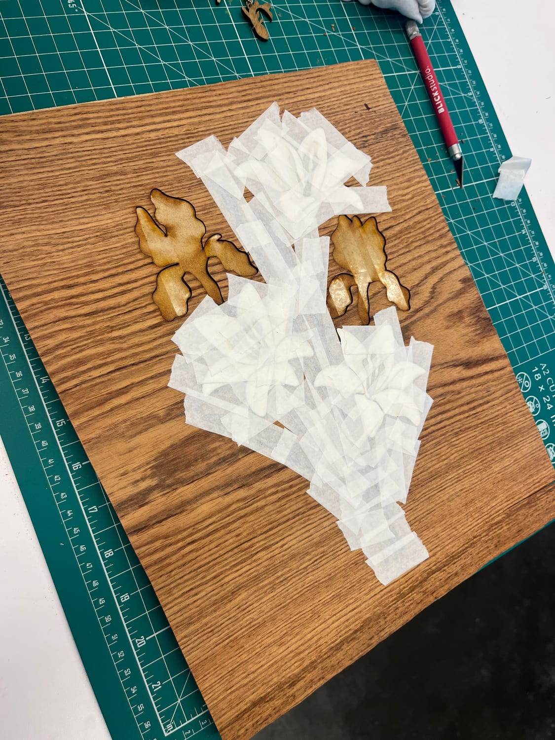 The taped-up lily heads on the cutting mat beside two loose laser-cut iris pieces, edges charred from the laser.