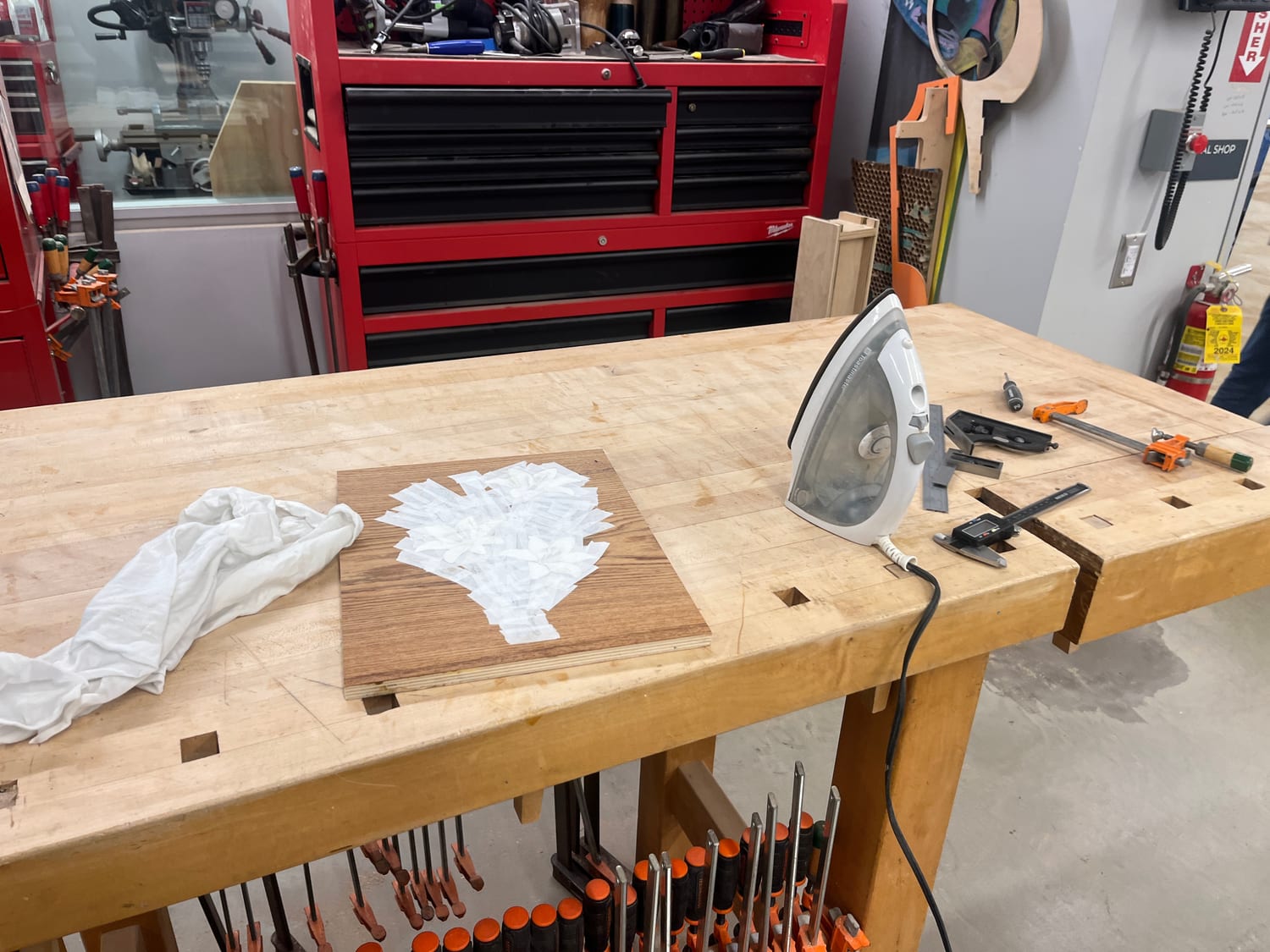 Gluing the veneer down on the shop bench — a household iron sets the glue through the veneer tape, calipers and clamps at hand.