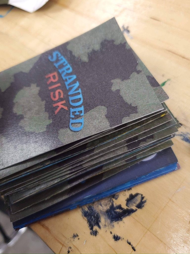 A hand-cut stack of the camouflage-patterned Stranded Risk cards on the workbench.